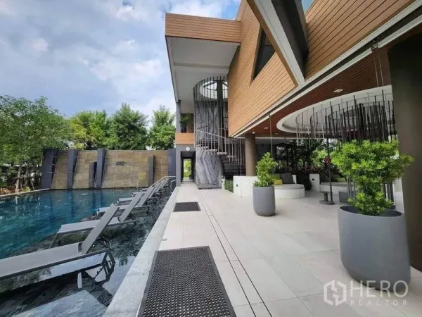 Detached House for sale in Sai Mai, Bangkok - Modern clubhouse with spiral staircase beside a long swimming pool with sun loungers and planters.