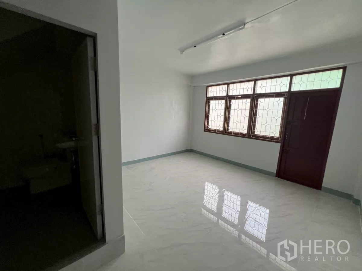 Shophouse for rent in Khlong Toei, Bangkok - Renovated room with glossy white floor tiles, grilled windows and attached bathroom door.