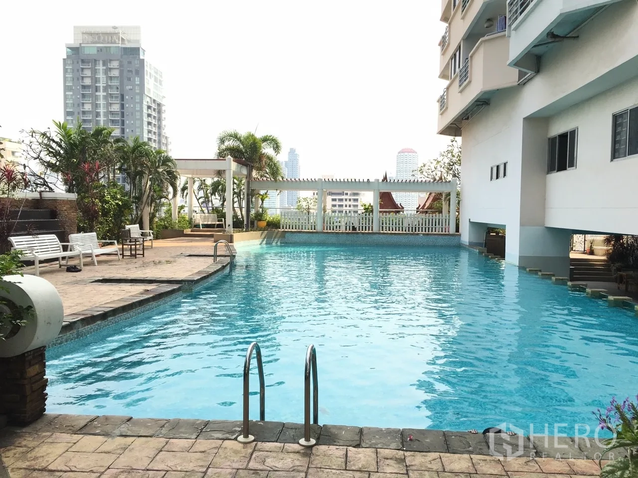公寓 出售在Khlong Toei, Bangkok - 公寓泳池，池畔座椅与绿植，背景为城市景色。