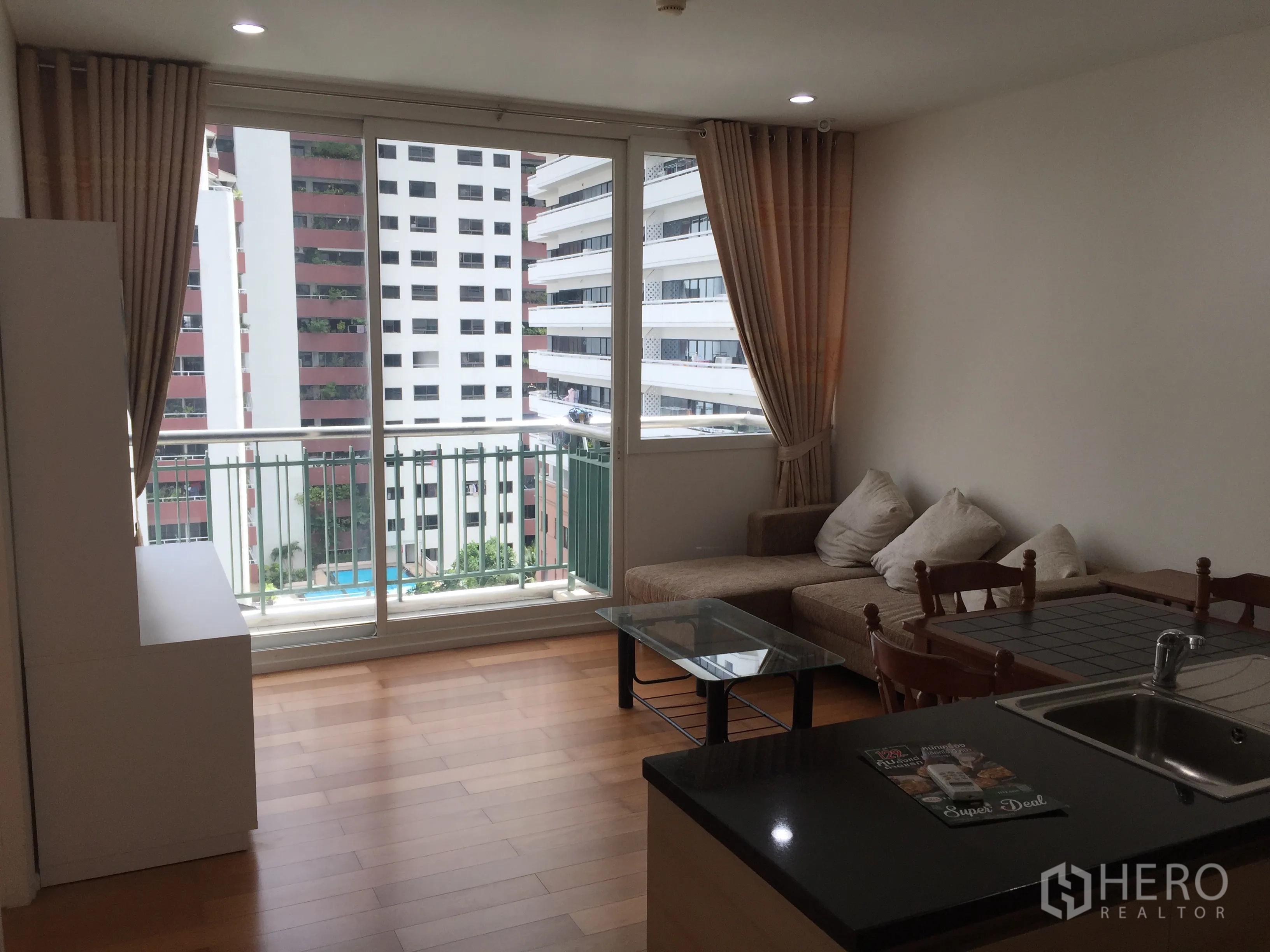 公寓 出租或出售在Watthana, Bangkok - 客厅连接阳台，转角沙发与城市景观，旁为开放式厨房。
