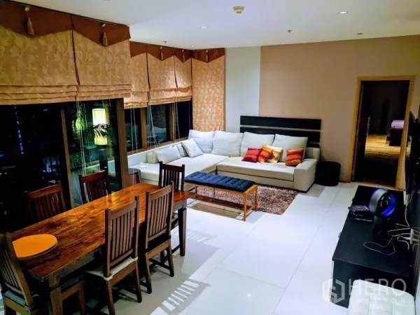 Condominium for rent - Open-plan living room with L-shaped sofa, wooden dining set, and large windows with Roman blinds at night.