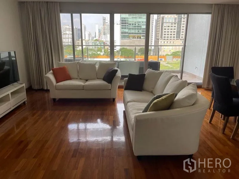 公寓 出租在Pathum Wan, Bangkok - 明亮客厅，双白色沙发、电视柜与大窗户，眺望城市景色。