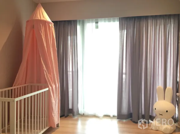 Condominium for rent in Khlong Toei, Bangkok - Bright bedroom with full-height curtains over balcony windows and a crib.