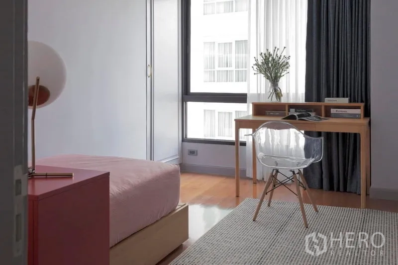 Condominium for sale in Watthana, Bangkok - Second bedroom with study desk by the window, acrylic chair and pink bedding.