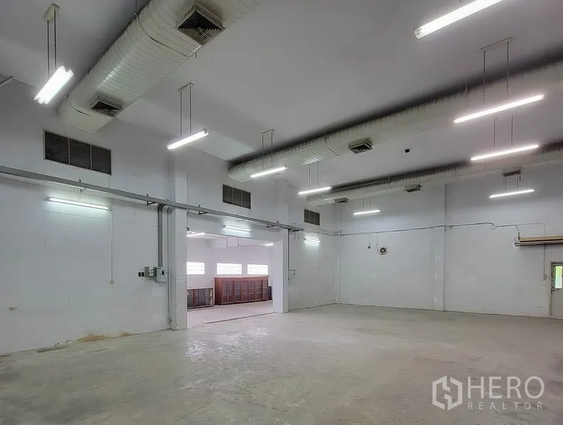 Warehouse for rent in Sam Phran, Nakhon Pathom - Warehouse hall with suspended ducts, bright lights and a side opening to an annex.