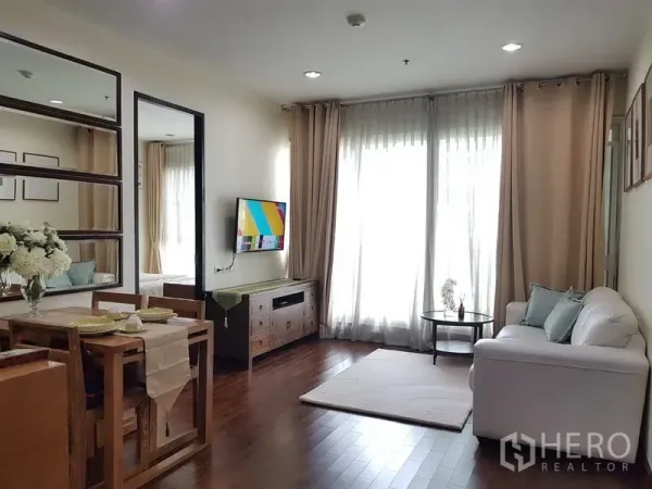 Condominium for rent in Pathum Wan, Bangkok - Bright living and dining area with wood floors, white sofa, wall-mounted TV and full-height curtains.