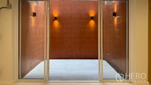 Home Office for rent in Watthana, Bangkok - Internal courtyard with terracotta wall and sconces viewed through sliding glass doors.