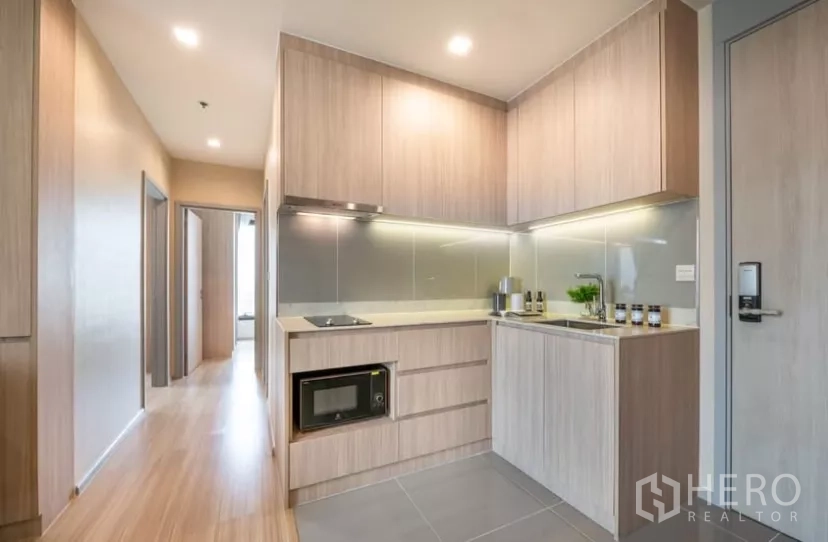 Condominium for rent in Chatuchak, Bangkok - L-shaped kitchen with electric hob, hood, microwave, ample cabinets and grey tile floor.