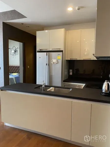 Condominium for rent in Watthana, Bangkok - Sleek kitchen with peninsula, black countertop, white cabinets and a double‑door refrigerator.
