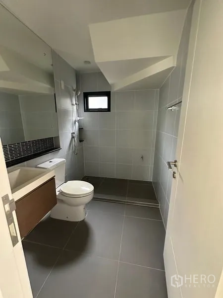 Detached House for rent or sale in Lam Luk Ka, Pathum Thani - Contemporary bathroom with toilet, wide mirror and a shower zone with gray tiles.