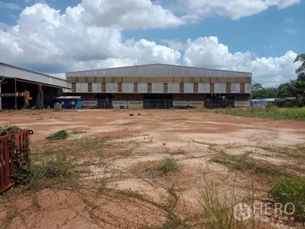 Factory for sale in Chachoengsao - Front view of an industrial warehouse facing a spacious red-earth yard and open working area.