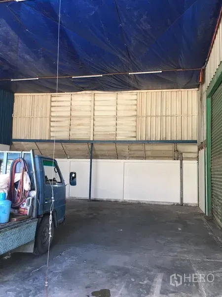 货栈 出租在Suan Luang, Bangkok - 有顶装卸区，配卷闸门和高檐棚，旁边停放小型卡车。