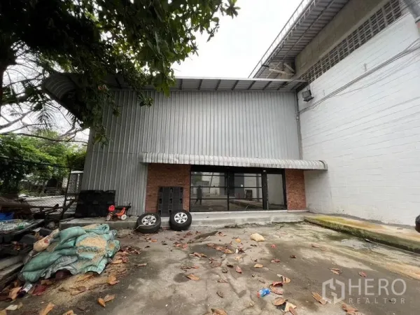 货栈 出租在Suan Luang, Bangkok - 曼谷Suan Luang仓库外观，金属波纹板立面与砖墙细节，玻璃入口及小型装卸前院。