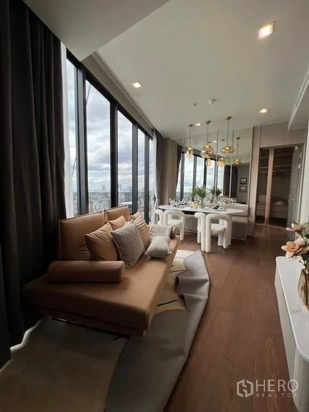 公寓 出租在Ratchathewi, Bangkok - 狭长客厅，沙发与吊灯上方的餐桌，旁为整面玻璃。