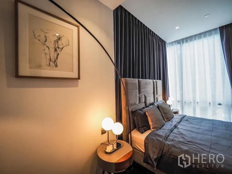 คอนโด ให้เช่าในPathum Wan, Bangkok - ห้องนอนหลักพร้อมหัวเตียงบุนุ่ม โคมไฟข้างเตียง และผ้าม่านสูงจรดเพดาน
