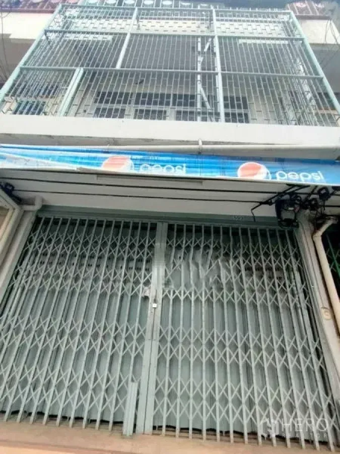 Shophouse for rent in Khlong Toei, Bangkok - Street-level view of a multi-storey shophouse with metal folding gate, balcony grilles and a blue awning in Khlong Toei near BTS Phrom Phong.