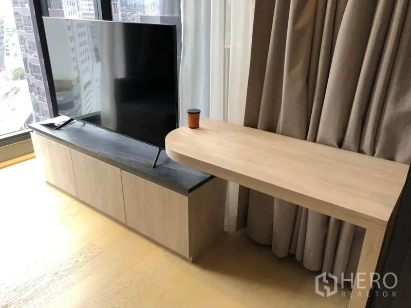 Condominium for rent in Din Daeng, Bangkok - Living area with TV on wood console and floating desk by floor-to-ceiling window.