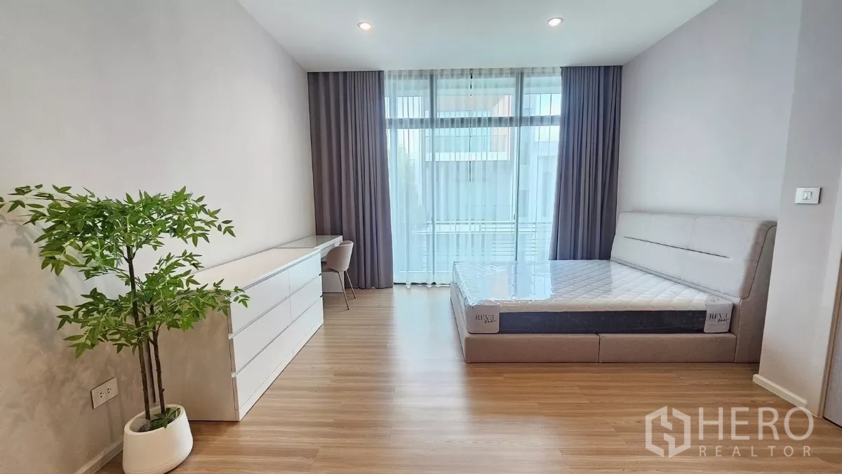 Townhouse for rent in Saphan Sung, Bangkok - Bright master bedroom with bed, long dresser, desk and balcony glazing.