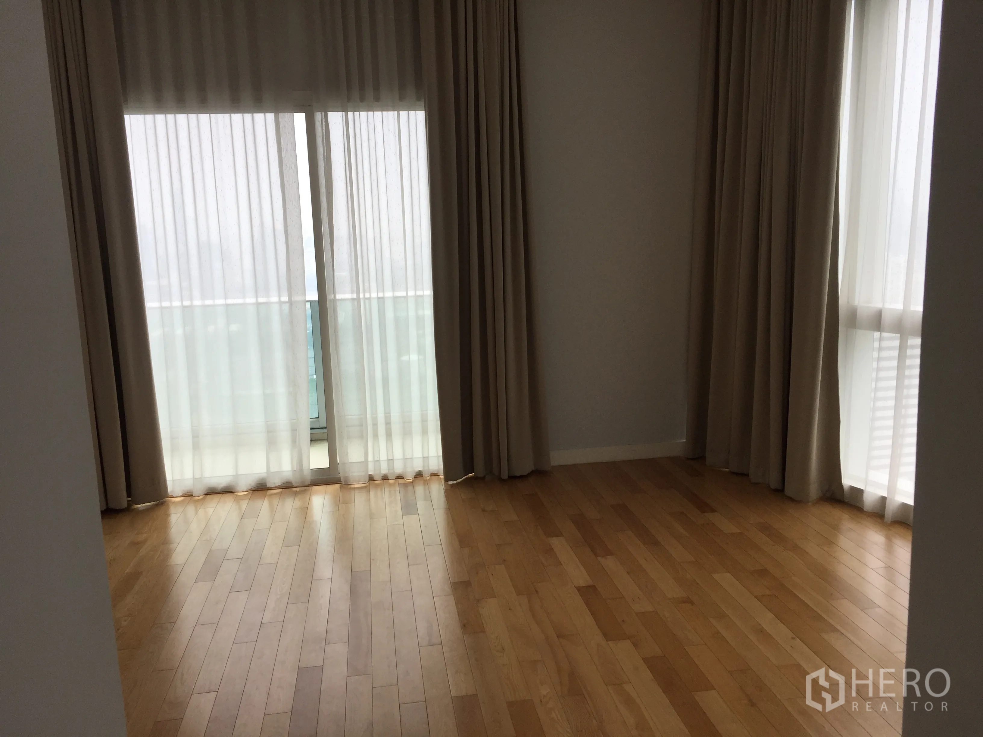 Condominium for rent in Khlong Toei, Bangkok - Bright bedroom with corner windows, floor-to-ceiling curtains, hardwood flooring and balcony access with city outlook.