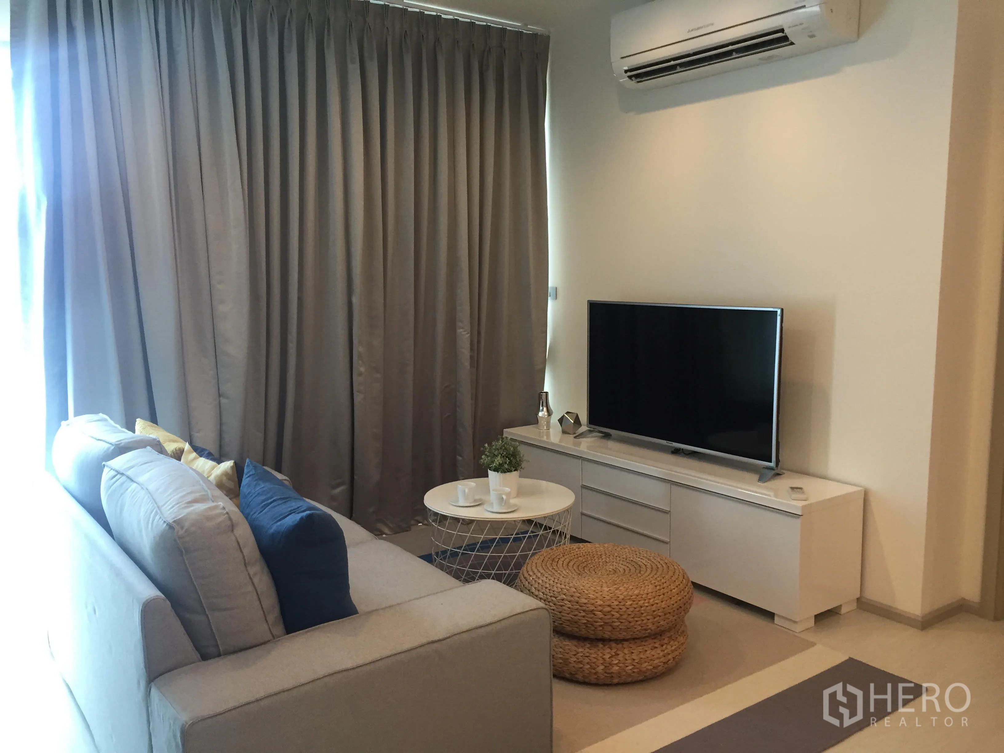 Condominium for rent in Khlong Toei, Bangkok - Cozy lounge with TV console, air conditioner and full-length curtains beside a round coffee table.
