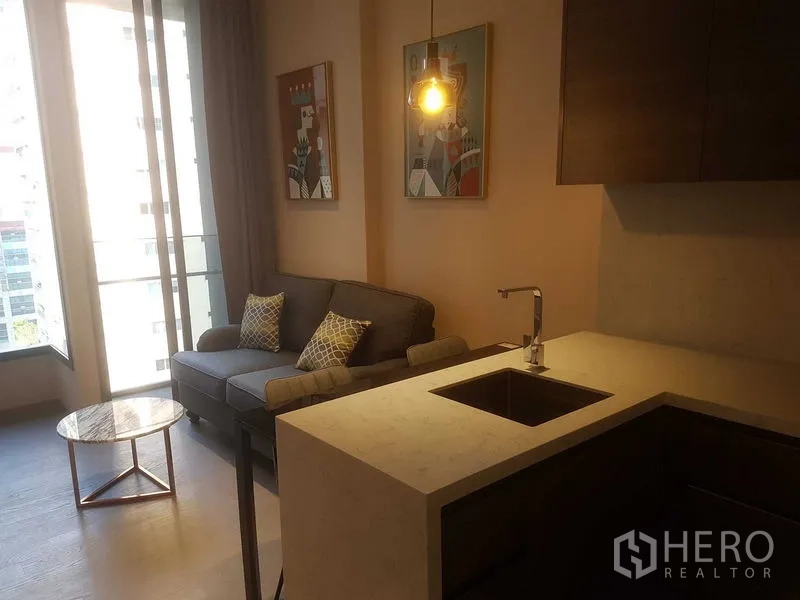 公寓 出租在Watthana, Bangkok - 起居区通往阳台，可观城市景观，旁为带岛台小厨房。