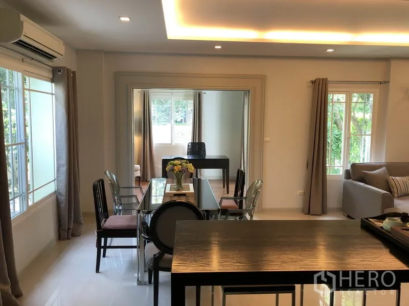 Detached House for rent or sale in Bang Kapi, Bangkok - Dining area with glass table and large windows next to a multipurpose room separated by sliding glass.