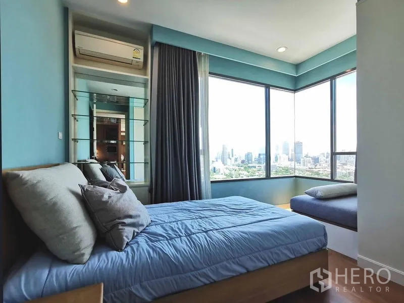 Condominium for rent in Sathon, Bangkok - Corner bedroom with panoramic windows, city views and a cushioned window seat.