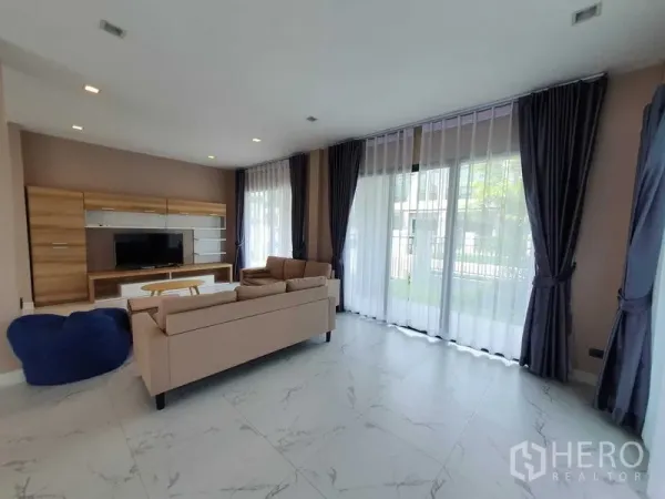 Detached House for rent in Khlong Luang, Pathum Thani - Sunlit living room with sheer curtains, sofa set and media wall facing a TV.