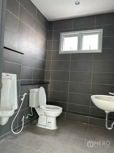 Factory for rent in Bang Sao Thong, Samut Prakan - Clean tiled restroom with toilet, urinal, sink and a small window for ventilation.