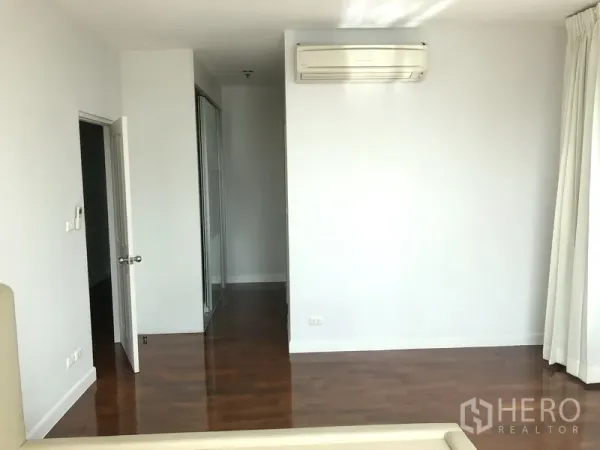 Condominium for rent in Khlong Toei, Bangkok - Sunlit bedroom with wood flooring, wall-mounted air conditioner, and full-height curtains.