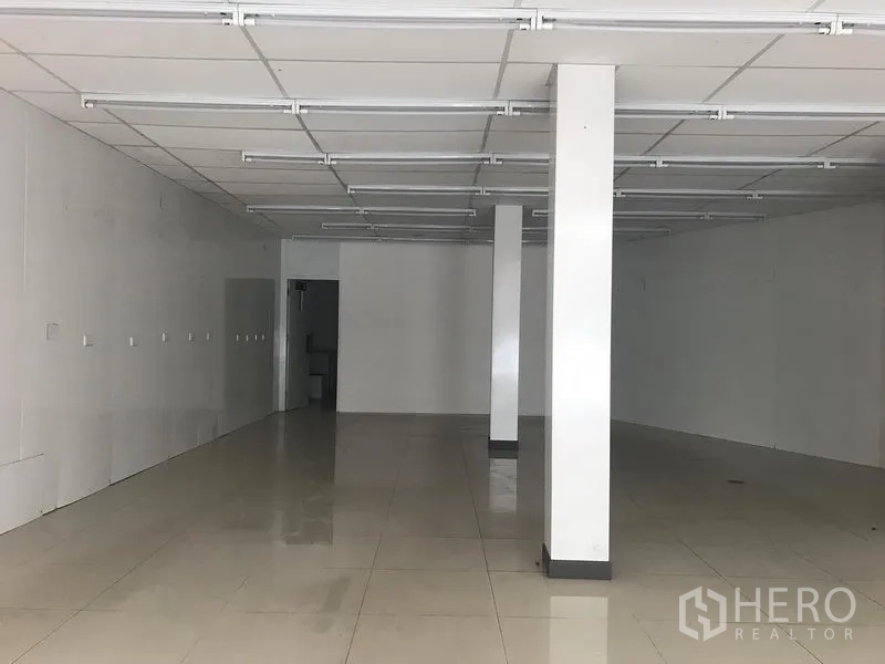 Retail Space for rent in Khlong Toei, Bangkok - Open-plan shop interior facing a rear access door, with white pillars, polished tiles and ceiling-mounted linear lighting.