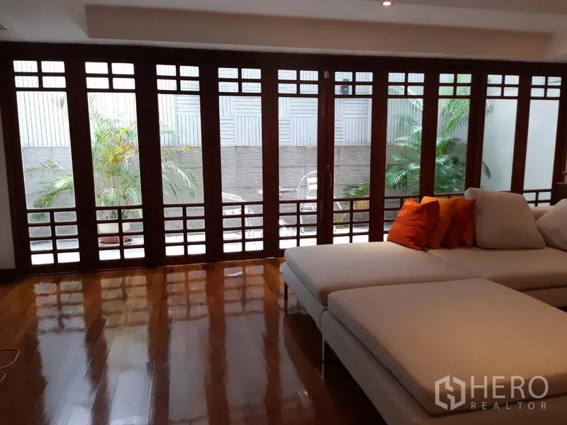 ทาวน์เฮาส์ ให้เช่าในWatthana, Bangkok - ห้องนั่งเล่นรับแสงพร้อมประตูบานกระจกกรอบไม้สูงจรดเพดาน เปิดออกสู่ลานส่วนตัวมีต้นปาล์มและโซฟามุม พื้นไม้เงางาม