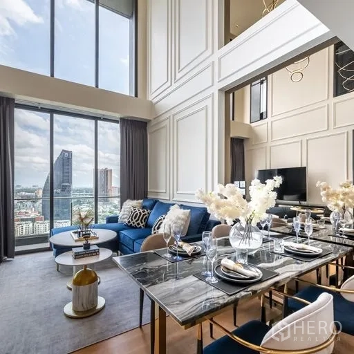 Condominium for rent in Khlong Toei, Bangkok - Elegant dining space set for six with a black marble table beside tall windows and a blue sectional in a bright loft.