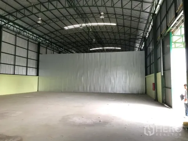 Warehouse for rent in Lat Krabang, Bangkok - Interior view toward a partition wall with large side doors, concrete flooring, and a wall-mounted fire extinguisher.