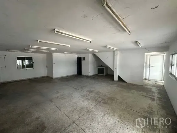 Factory for rent in Nonthaburi - Empty ground-floor office area with fluorescent lighting, concrete floor and staircase to upper level.