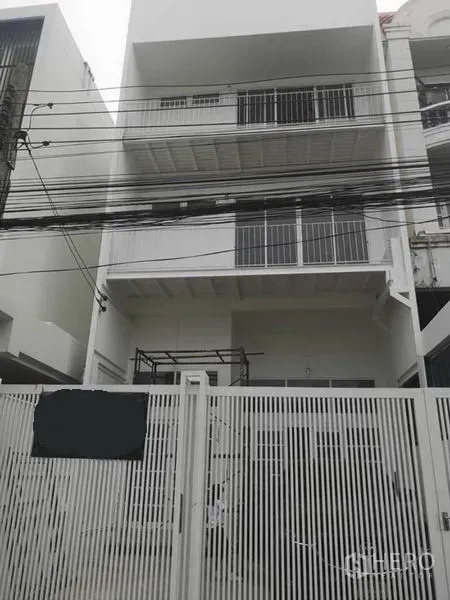 Townhouse for rent or sale in Din Daeng, Bangkok - Front facade of a multi-storey white townhouse with metal gate and balconies on an urban street.