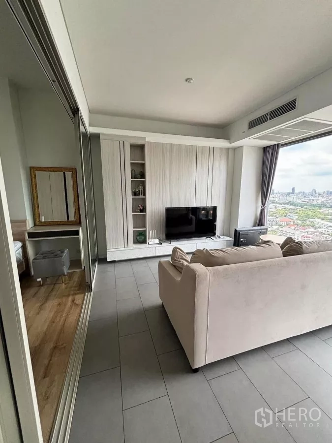 Condominium for rent or sale in Phaya Thai, Bangkok - Living area with built‑in TV wall and large window, connected to a bedroom by a sliding glass door.