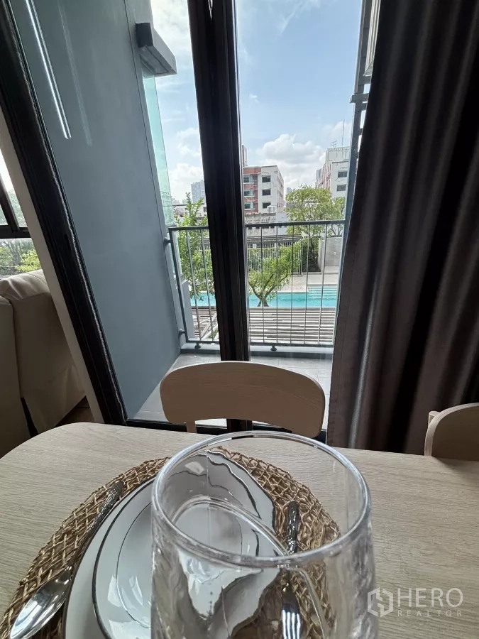 公寓 出租在Phra Khanong, Bangkok - 餐区阳台门开启，俯瞰小区游泳池。
