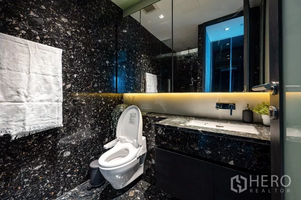 Condominium for rent or sale in Khlong Toei, Bangkok - Luxurious bathroom with black marble walls, backlit vanity and modern toilet.