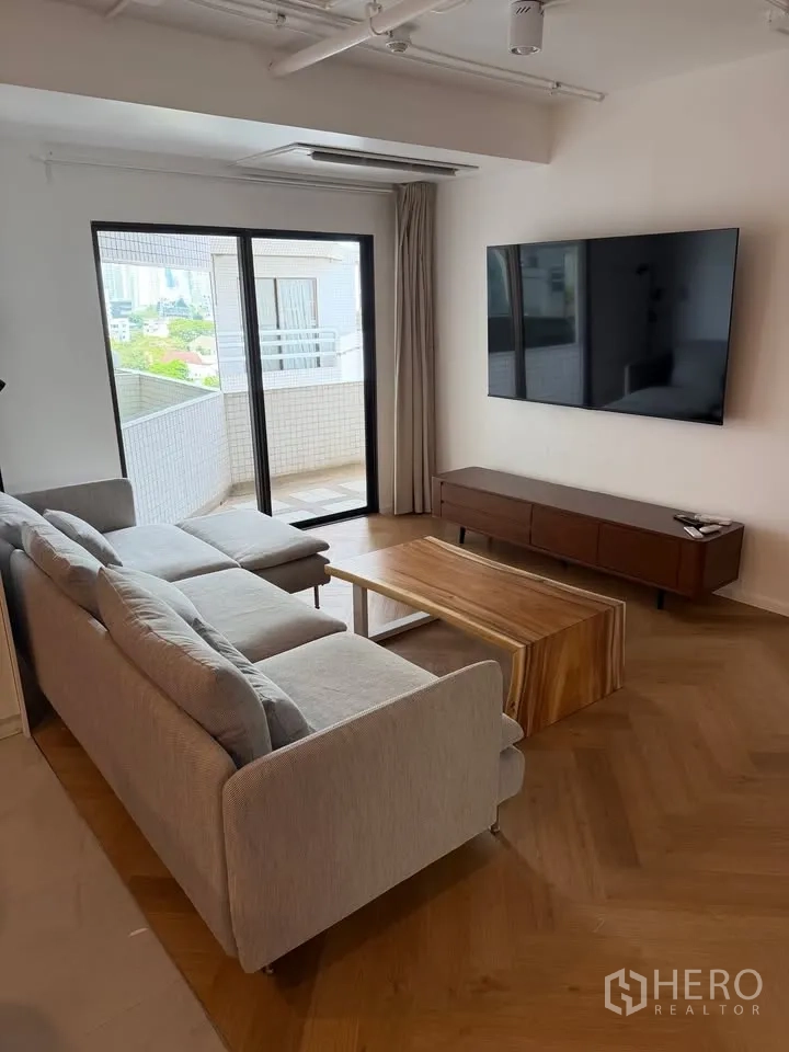 公寓 for rent in Watthana, Bangkok - 客厅沙发面对墙挂电视，侧面为通往阳台的门。