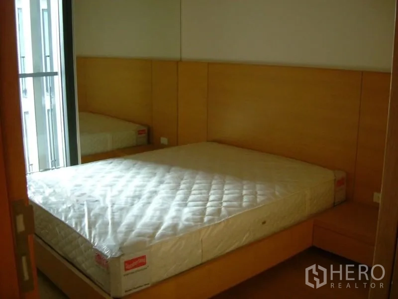 Condominium for rent in Sathon, Bangkok - Second bedroom with queen bed, wood headboard, mirrored wall, and sliding window.