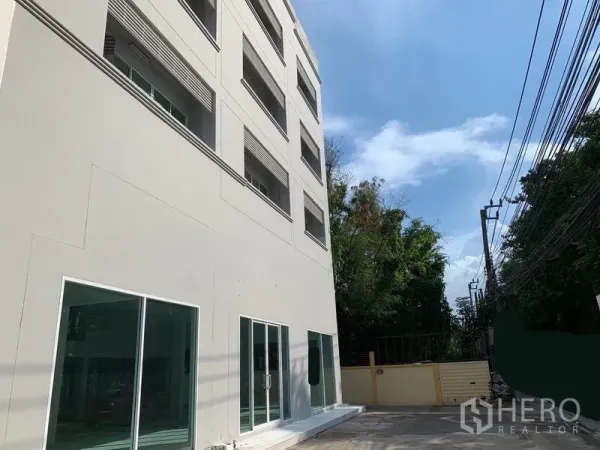 Office Space for rent in Huai Khwang, Bangkok - Side view of the office building with glass storefronts along a quiet lane lined with power cables and trees.