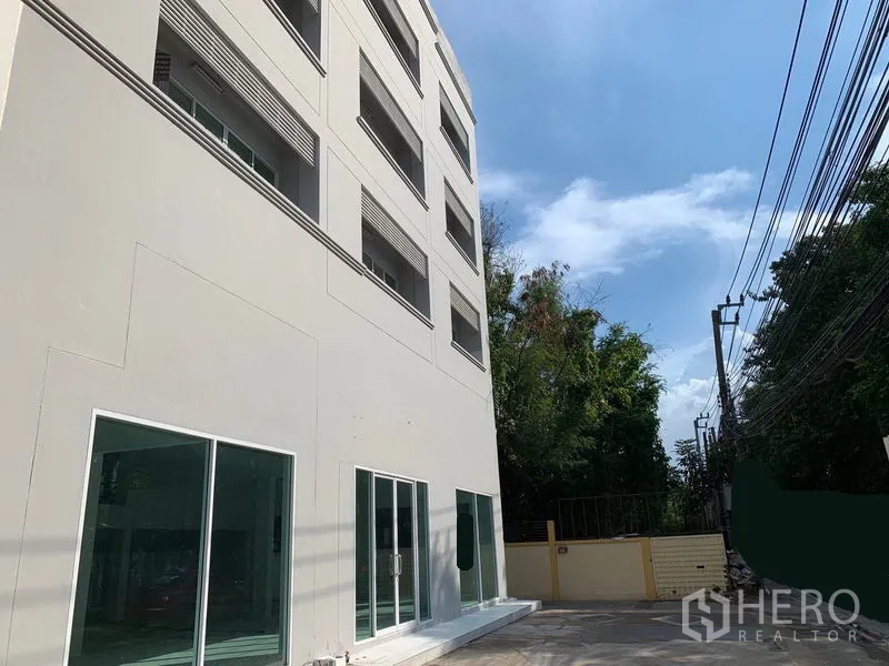 Office Space for rent in Huai Khwang, Bangkok - Side view of the office building with glass storefronts along a quiet lane lined with power cables and trees.