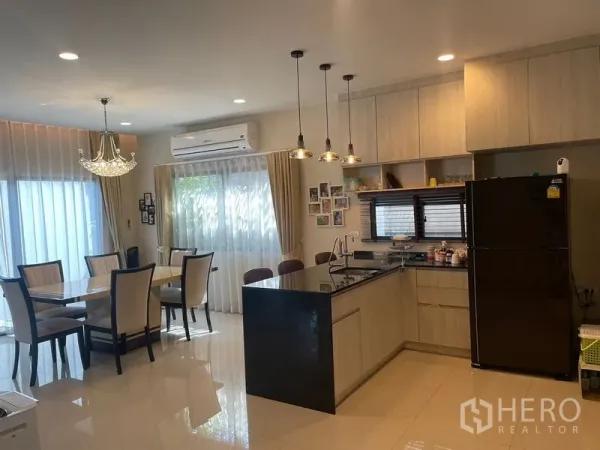 Detached House for rent or sale in Lam Luk Ka, Pathum Thani - Bright dining area and Western kitchen with black stone island, pendant lights and light wood cabinetry.
