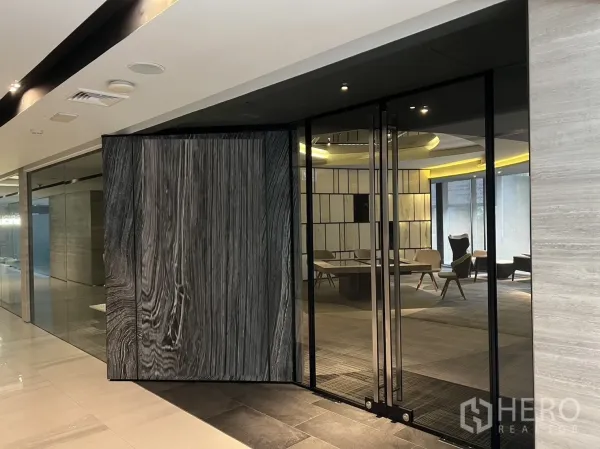 Retail Space for rent in Watthana, Bangkok - Glass-front retail entrance with a large pivot wood door opening into a sleek showroom with seating.