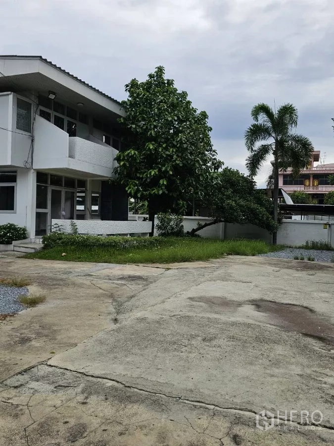 Detached House for rent or sale in Lat Phrao, Bangkok - Closer view of the house with lawn, mature trees, and spacious paved yard.