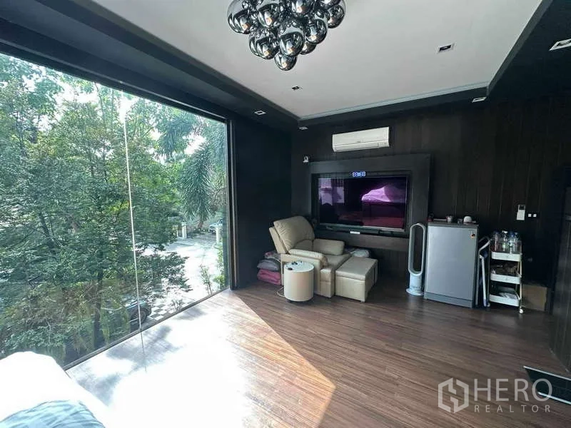 独立式住宅 出售在Suan Luang, Bangkok - 主卧一角，巨屏电视、躺椅与迷你冰箱，超大玻璃窗看花园。