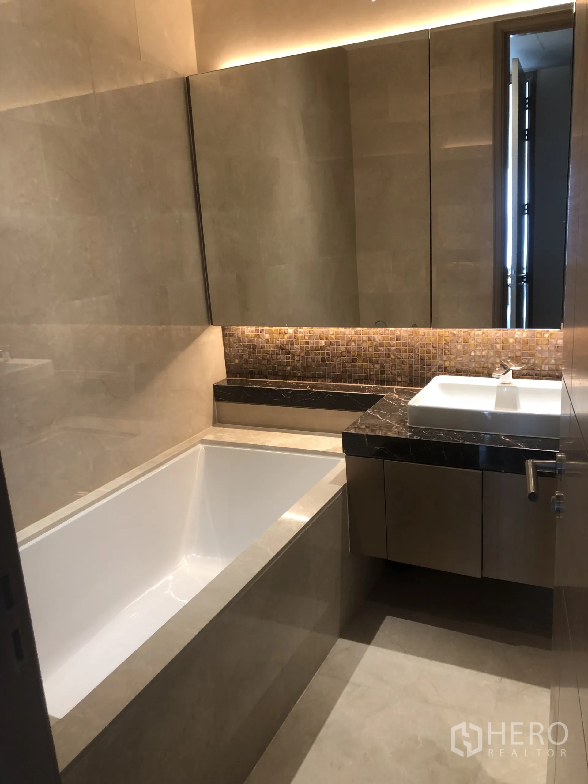公寓 出租在Pathum Wan, Bangkok - 浴室设深浸浴缸、大理石洗手台与大面积镜柜，灯光温暖。