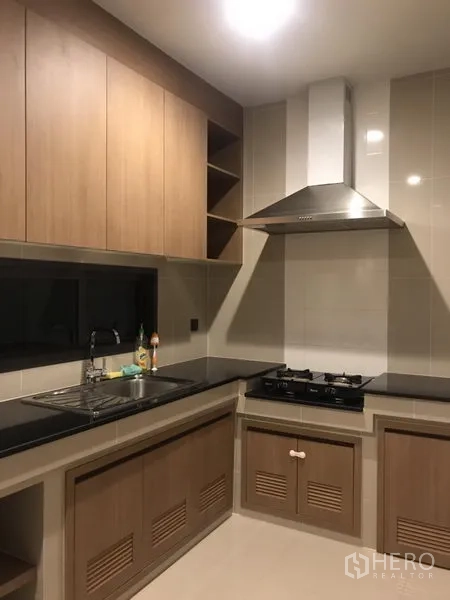 Detached House for rent in Bang Kapi, Bangkok - Built-in L-shaped kitchen with gas hob, range hood, sink and wood cabinetry.