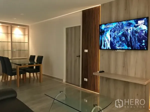 Condominium for rent in Watthana, Bangkok - Modern living and dining area with wood feature TV wall, glass coffee table, and built‑in display shelves.